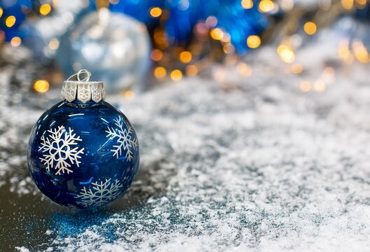 New Year background with space for text. Blue Christmas tree toy lies on snow against the background of New Year tinse