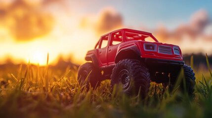 Fototapeta premium A red toy car, perfect for off-road adventures, zips through grassy fields at sunset. It's a four-wheel drive vehicle, ready for extreme rides and rallies.