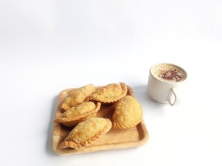 Pastel cake, a traditional Indonesian snack. Served on a woven bamboo wooden plate and a cup of black coffee. On a white background