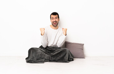 Caucasian man in pajamas sitting on the floor at indoors celebrating a victory in winner position