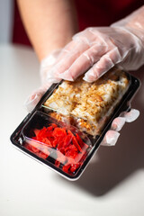 Woman in gloves packaging sushi in plastic box. Plastic containers for food delivery. Using plastic for packaging. Food in disposable dishes.