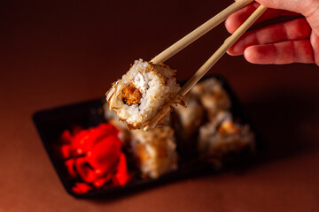 Chopsticks taking portion of sushi roll. Sushi rolls with salmon cream cheese and cucumber in take away package. Food delivery concept.