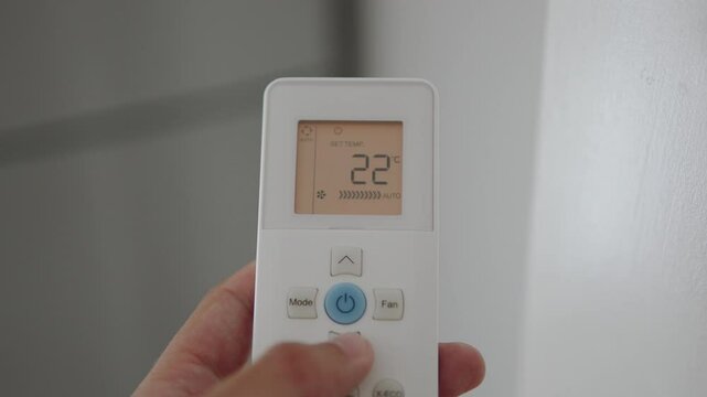 Man reduces temperature of air conditioner on control panel close up. Adjusting operation of split system on hot day for cooling and pressing buttons with fingers on remote control with LCD screen.