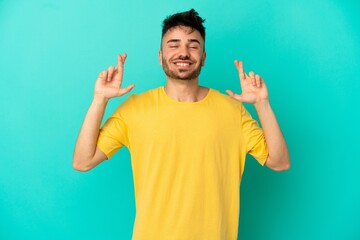 Young caucasian man isolated on blue background with fingers crossing and wishing the best