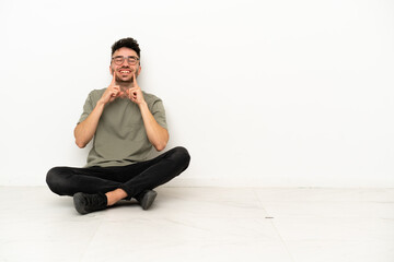 Young caucasian man sitting on the floor isolated on white background smiling with a happy and pleasant expression