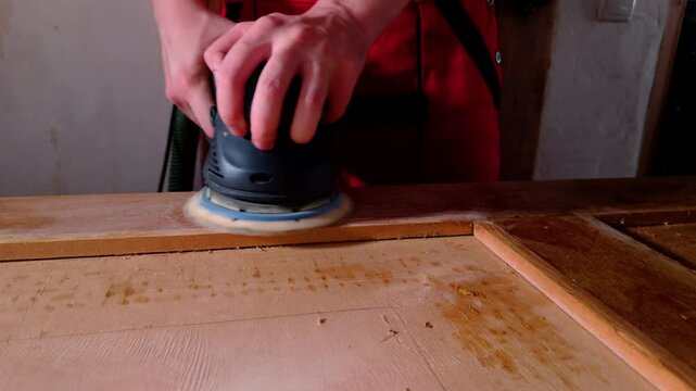 Carpenter with sander polishes door moving disc in circle