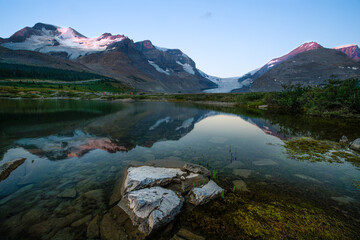 The panoramic view of snowy mountain and colorful clouds with lake reflections at ice field center of Jasper National Park. Famous Athabasca glacier in Canada at dawn.