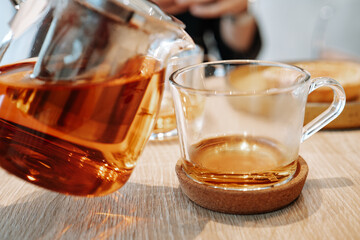 A glass teapot filled with tea being poured into a cup.