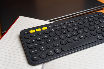 Flat lay of a notebook, a bluetooth keyboard and a computer on a wooden desk. Working from home and digital transition concept.