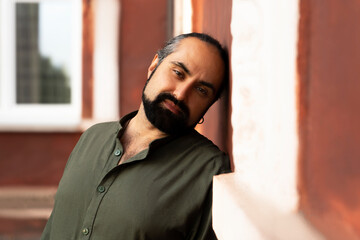 Artistic portrait of a bearded dark-haired man in a green shirt against a burgundy wall. Side view. High quality photo