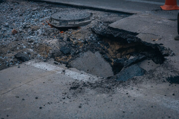 A big hole in the concrete floor. A huge hole in the road. Dangerous for traffic. ra in the ground in the middle of the road. Asphalt that has fallen into the ground