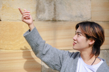 手を掬い上げるように上げて壁の前に立っている日本人男性