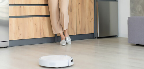 Young woman using automatic vacuum cleaner to clean the floor, controling machine housework robot