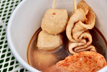 Oden fish cake sticks with soup in white paper bowl isolated on horizontal white metal table surface background.