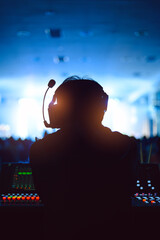 Silhouette of a sound technician wearing a headset, working at a control panel during a live event. The background features blue stage lighting and a blurred audience, creating a vibrant atmosphere.