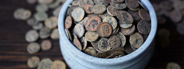 Roman coin hoard on dark wooden table, Ancient money in old ceramic pot, wide banner for vintage background. Concept of pile, antique, texture, civilization © scaliger