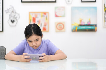 asian child playing game on smartphone or kid girl holding looking mobile phone and addicted to hyperactive ADHD or people fun relax watching phone and technology learning on white with copy space