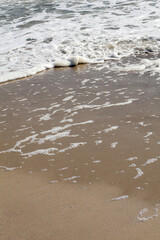 Close-up of ocean foam and ripples delicately covering golden sandy beach, capturing the serene meeting of water and land