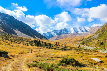 Mountain bikers exploring scenic mountain valley trail with snow-covered peaks and golden autumn meadows. Tian Shan mountains, Almaty, Kazakhstan