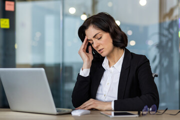 Businesswoman looks stressed at office desk with laptop. Experiencing pressure and tension in professional setting. Concept of workplace stress, challenges, and corporate resilience. Managing emotions