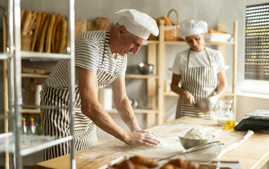 Elderly man and woman kneading and whipping dough