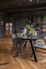 Close-up of a chic luxury dining table in a dark brutal interior in a historical style in a mansion with panoramic windows. grey-green walls and brown parquet