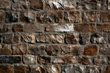 Close-up of a rough stone wall with irregular dark brown and gray bricks, natural texture background.  