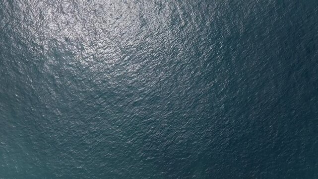 Sunlight reflects on a deep blue water surface, creating a shimmering effect with small waves dancing across the scene