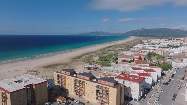 Aerial view of Tarifa's coastal townscape, featuring beaches, rooftops, and the Strait of Gibraltar with Morocco visible across the water.