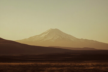 A photograph of the silhouette of an alpine mountain with snow on top, taken from a distance, against a light gray sky. 2