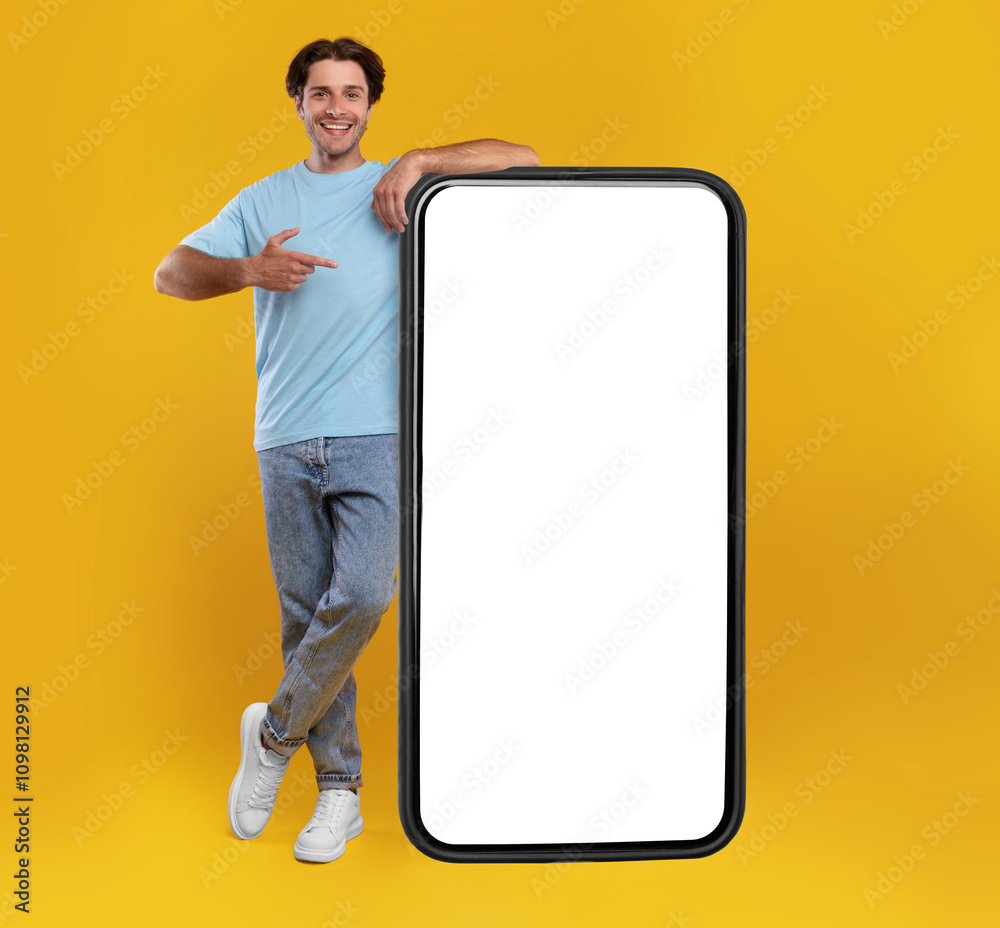 Poster Check This Website. Smiling male leaning on smart phone with white blank screen, showing device and pointing finger at gadget with empty free copy space for mock up, recommending app, full body length