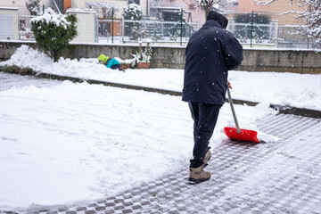 Person clearing snow with red shovel in winter urban scene. World Snow Day. Snowstorm and natural disasters and snowfalls. © dargog