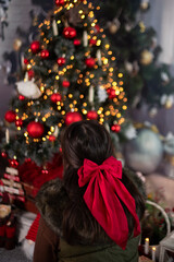 Dark-haired girl with red ribbon in front of a Christmas tree with light