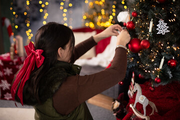 Dark-haired girl with red ribbon in front of a Christmas tree with light