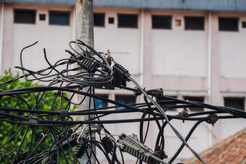 Close-up view of a tangled mass of electrical wires and cables on a utility pole against a blurred...