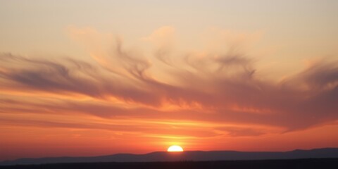 Obraz premium A golden sun sets behind a horizon painted with soft, ethereal clouds, the sky a tapestry of warm colors.