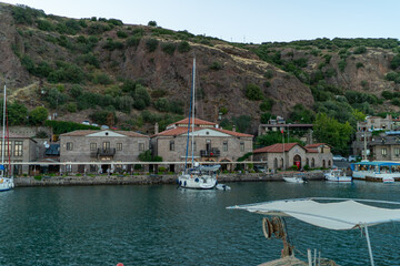 Fototapeta premium Scenic View of Assos Harbor with Stone Houses, Boats, and Aegean Sea on a Sunny Day, Turkey