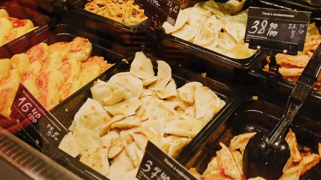 Close-up of traditional Ukrainian dumplings with potato filling and zrazy displayed in black trays with price tags at a food counter. Varenyky with potato. Street food