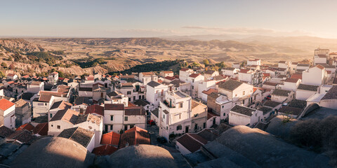 Ancient town on hill side with levels of whitewashed houses and tiled roofs at sunset, Pisticci,...