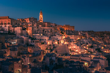 Panoramic view of ancient city on hill side with many levels of houses at night, Matera, Italy