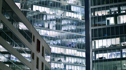 Obraz premium Office building in the evening with lightened workspaces. Modern, glazed skyscraper in financial district. Late hours in the office.