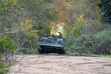 large green tracked tank recovery vehicle amongst woodland cover