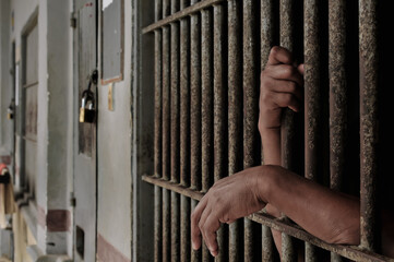 hands of a prisoner behind prison bars on black background	
