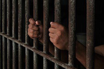 Obraz premium hands of a prisoner behind prison bars on black background 