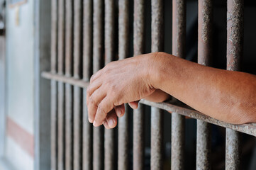 hands of a prisoner behind prison bars on black background	
