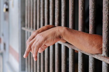 hands of a prisoner behind prison bars on black background	

