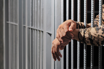 hands of a prisoner behind prison bars on black background	
