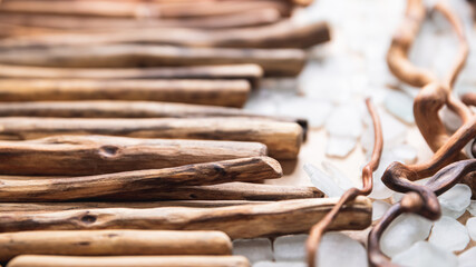 Straight driftwood branches arranged in a row with curved pieces stacked nearby, complemented by scattered sea glass. A balanced composition highlighting natural textures and rustic craftsmanship