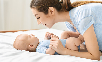 Speech and language development for babies. Young mother playing with her cute newborn baby in bed,...
