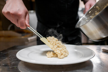 A chef gracefully plates creamy risotto from a pan onto a white dish, with steam rising, showcasing...